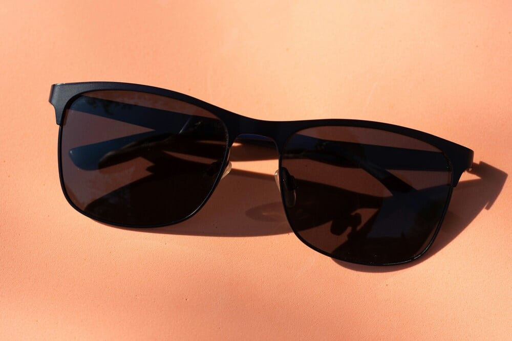 black sunglasses A close-up shot of newly repaired matte black sunglasses laying flat against a solid peach-colored background