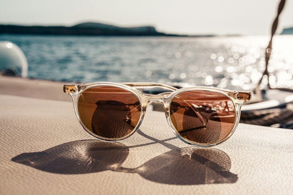 white sunglasses A pair of newly repaired transparent, clear-frame sunglasses resting on the deck of a boat with bright ocean water behind them
