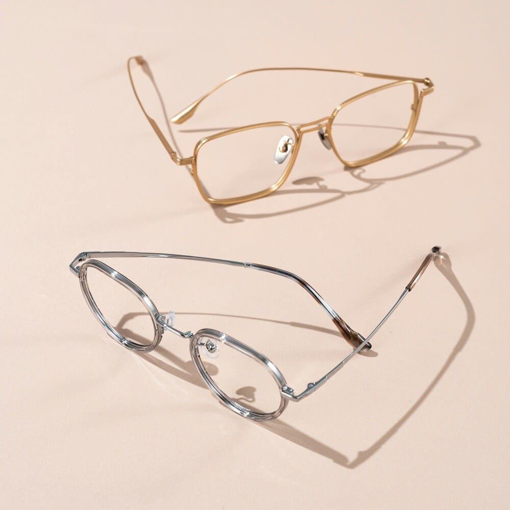 titanium eyeglasses on the sand Two pairs of metallic eyeglasses resting on a solid beige background.