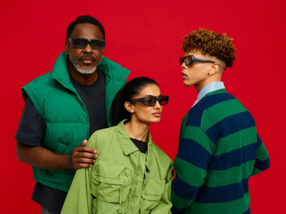varied styles of sunglasses for men and women A group of three people wearing different stylish sunglasses against a bright red background.