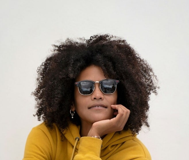 woman in yellow shirt wearing sunglasses A smiling woman with an afro hairstyle wearing a yellow hoodie and sleek black sunglasses.